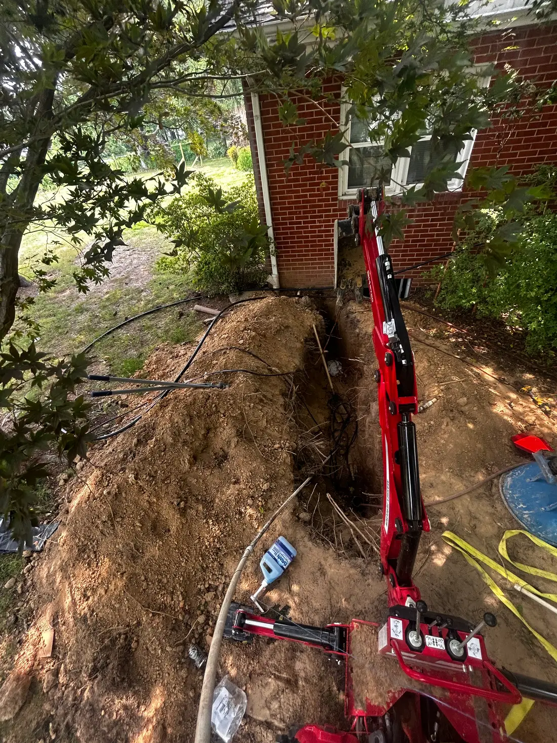 Massey Ferguson compact backhoe digging a drainage trench along a brick home foundation in Maryland