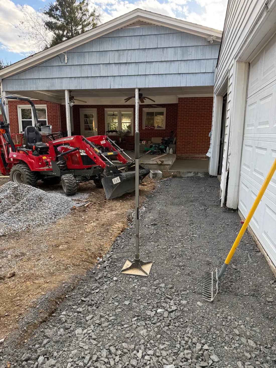 Compact tractor with front-end loader spreading fresh gravel at a residential garage entrance in Maryland