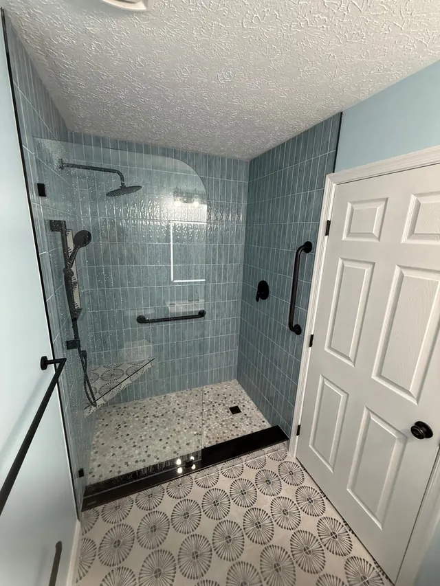 Walk-in shower with vertical stacked blue tile, frameless glass, and patterned floor tile after bathroom remodel in Severn MD