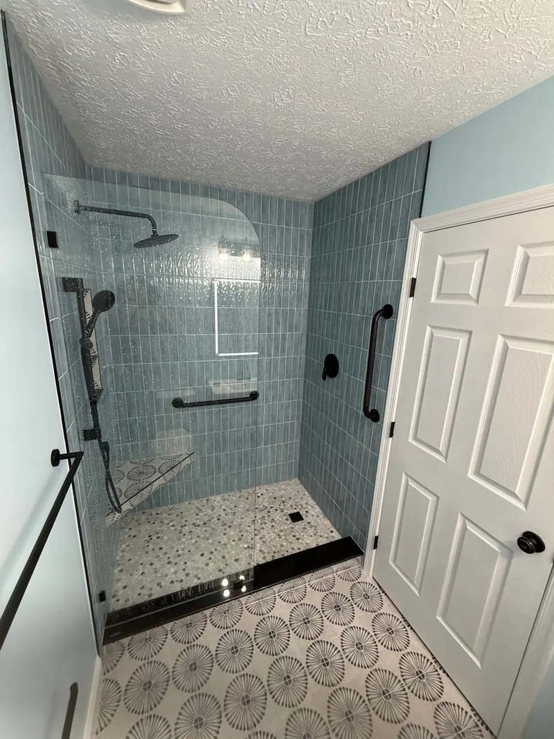 Walk-in shower with vertical stacked blue tile, frameless glass, and patterned floor tile after bathroom remodel in Severn MD